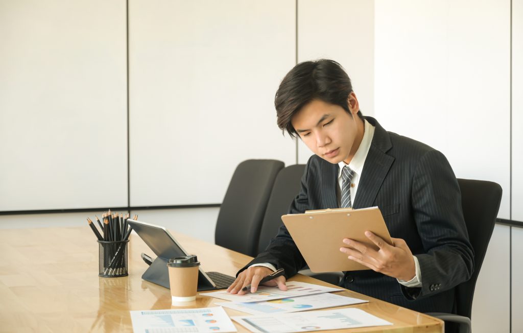 Young Asian man in a suit sitting at a desk and reviewing documents